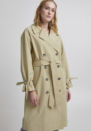 Beige trench coat med dobbelspent design, stor krage og kortede ermer med bånd. Har dekorative knapper og belte i midjen.