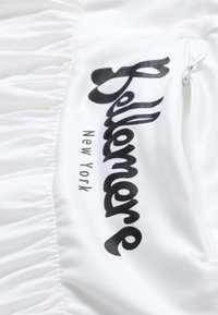 Tissu blanc avec des sections froncées présentant un texte noir "Felllemore New York" et une fermeture éclair blanche sur le côté droit.