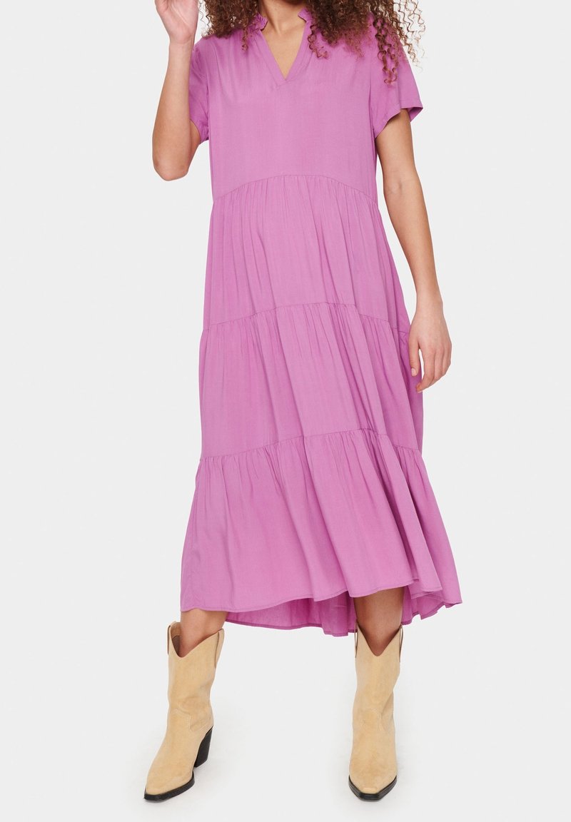 Rosa knälång klänning med korta ärmar, V-ringning och flikig kjol. Bärs med ljusbruna cowboyboots. Mjuk tyg och flytande design.