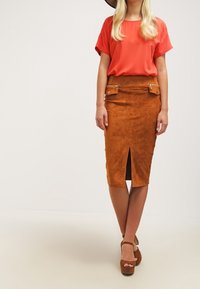 Orange kortärmad blus i kombination med en brun mocka penkjol med framfickor och silverdetaljer. Bruna plattformsskor.