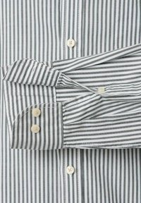 Witte shirt met dunne zwarte verticale strepen, met een knopenfront en een mouwmanchet met twee knopen.