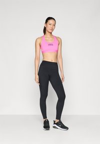 Roze sportbeha met een logo, gecombineerd met zwarte leggings en zwarte sportschoenen. De outfit heeft een eenvoudig, aansluitend ontwerp.
