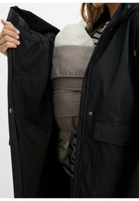 Giacca nera impermeabile aperta, che mostra un marsupio grigio con una texture morbida e un motivo leggero, che tiene un inserto per neonati bianco.
