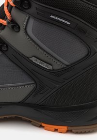 Vedenkestävä harmaa ja musta vaelluskengä, jossa on teksturoitua materiaalia, oranssit nauhat ja suojavarusteet nilkkatuen lisäämiseksi.