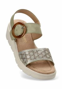 Sandalia cuña verde claro con una gran hebilla circular marrón, una correa plateada con corte floral y una plantilla suave beige. Suela texturizada.