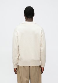 Pull en tricot beige clair avec un grand col, des poignets et un ourlet côtelés, présentant une coupe décontractée et une texture douce. Vue de dos affichée.