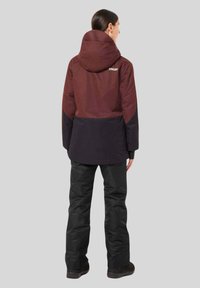 Maroon and black waterproof jacket with a hood, featuring a smooth texture and logo detail on the upper back, paired with black pants.