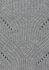 Tissu gris tricoté avec un motif texturé présentant des mailles diagonales et de petites ouvertures, mettant en valeur la qualité douce et volumineuse du fil.