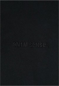 Fekete bordázott anyag, amelyen a "9N1M SENSE." felirat hímzett, azonos színben, így diszkrét kontrasztot képez a felületen.