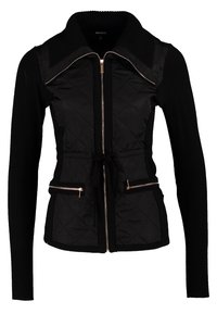 Veste noire matelassée à manches longues, avec fermeture éclair devant, taille à cordon, deux poches zippées et large col.