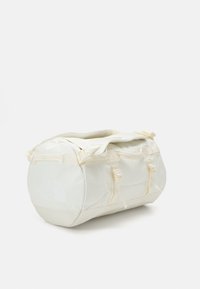 Sac de sport blanc avec des sangles ajustables, plusieurs poches zippées et un grand logo. Fabriqué en tissu résistant et texturé pour une utilisation en extérieur.
