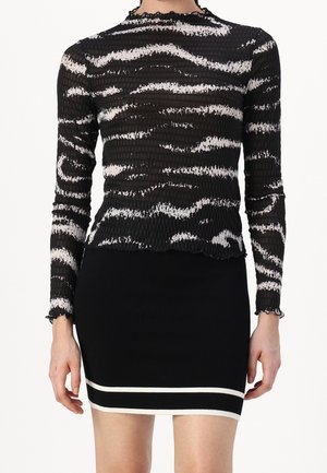 Kvinde iført en sort og hvid stribet langærmet tekstureret top kombineret med en sort mininederdel med to hvide horisontale striber.