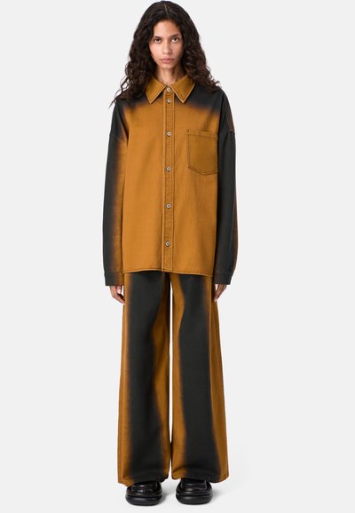 Übergroße Jacke und Hosen-Set in zwei Farben. Die Jacke verfügt über eine braune und schwarze Färbung, einen großen Kragen, Druckknöpfe und eine aufgesetzte Tasche.