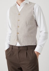 Brown and beige checked waistcoat with five buttons, worn over a white shirt, paired with brown trousers featuring side pockets.