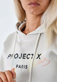 Lichtgrijze hoodie met zwarte "PROJECT X" tekst en multicolored cursieve "Paris" borduursel. Inclusief trekkers en een zachte stoftextuur.