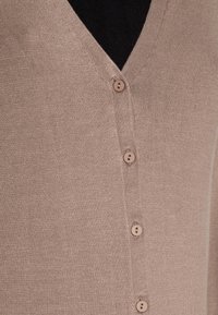 Ljusbrun stickad cardigan med fem matchande knappar över en svart ribbad topp.