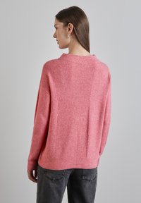 Roze gebreide trui met geribbelde structuur en drop shoulders, met een brede halslijn en een naaddetail op de rug, gecombineerd met donkergrijze jeans.
