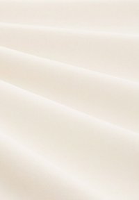 Tejido de algodón en un suave tono beige cremoso con una superficie ligeramente texturada, que presenta suaves caídas y pliegues.