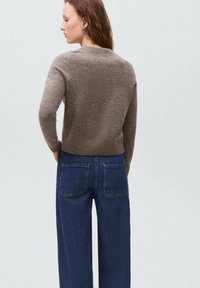 Brauner Strickpullover mit rundem Ausschnitt und geripptem Saum, getragen über hochgeschnittenen dunkelblauen Weitbeinjeans mit zwei Gesäßtaschen.