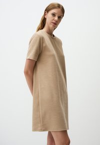 Beige Kurzarmkleid mit lockerer Passform. Hergestellt aus weichem Stoff, verfügt über einen runden Halsausschnitt und einen geraden Schnitt, der bis zur Mitte des Oberschenkels reicht.