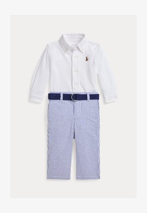 Chemise blanche à manches longues avec col à boutons, associée à un pantalon rayé bleu et blanc et une ceinture bleu marine, avec un petit logo sur la poitrine.