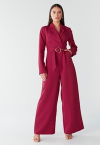 Bordeaux jumpsuit met een op maat gemaakte uitstraling, lange mouwen en een ceintuur in de taille. Glad materiaal, brede pijpen en een reverskraag ontwerp.