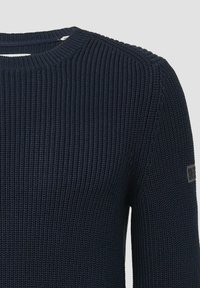 Marineblauer Strickpullover mit einem strukturierten Rippenmuster, rundem Ausschnitt und einem kleinen Markenlabel am Ärmel.