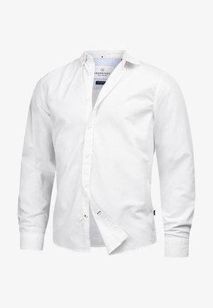 Hvit langermet skjorte laget av bomull med knapp-ned krage, med en subtil logo og avrundet kant. Teksturert materiale og enkel design.