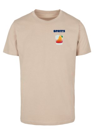 Bež pamučna majica s grafikom koktel čaše s narančinom kriškom i riječju "SPRTIZ" u plavoj boji iznad dizajna.