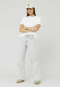 T-shirt en coton blanc, jeans large gris clair, baskets vertes et casquette beige avec une lettre noire "B" à l'avant.