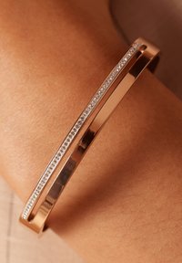 Roze gouden manchettenarmband met een glad oppervlak en een rij kleine, heldere edelstenen in het midden gezet.