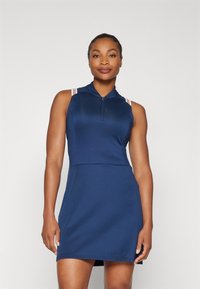 Robe de sport bleu marine avec un col zippé, sans manches et des bretelles de couleur claire. Tissu lisse et coupe ajustée.