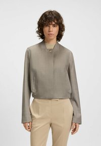 Gekürzte, grau karierte Jacke mit langen Ärmeln, Stehkragen und Knopfverschluss, kombiniert mit beigen Hosen. Glatte Textur.