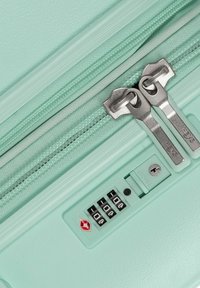 Valigia verde menta con un esterno texturizzato, doppi zippere argentati e una serratura a combinazione con foratura per la chiave per una maggiore sicurezza.