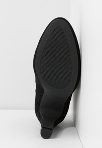 Suela de zapato de tacón alto de ante negro con una superficie lisa y texturizada y punta afilada. Presenta un tacón ligero y un agarre de goma para tracción.
