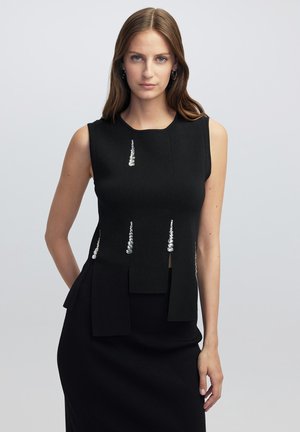 Top sin mangas de color negro con un diseño estructurado. Presenta adornos verticales y un dobladillo en capas. Fabricado con una tela texturizada.