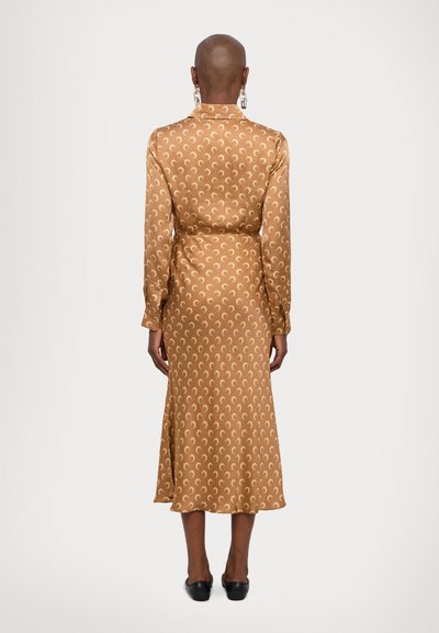 Long-sleeve, midi dress in a gold satin fabric featuring a cream crescent pattern. It has a fitted waist and flares gently at the hem.