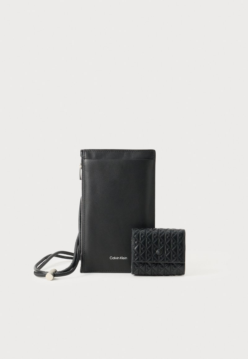 Pochette a tracolla in pelle nera con zip e manico, abbinata a un piccolo portacarte testurizzato con chiusura a scatto. Entrambi di Calvin Klein.