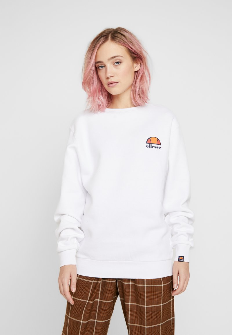 Sudadera blanca con cuello redondo, mangas largas y logotipo bordado. Tejido cálido con un corte holgado, combinada con pantalones de cuadros.