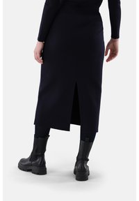 Marineblaue Woll-Midi-Rock mit einem Schlitz hinten, kombiniert mit schwarzen klobigen Stiefeln. Augenmerk auf der glatten Textur und klaren, einfachen Linien.