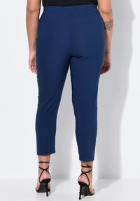 Pantaloni blu navy con un design aderente, texture liscia e taglio alla caviglia. Accompagnati da sandali neri con tacchi alti e cinturini.