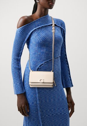 Beige Leder-Crossbody-Tasche mit Verschluss, mit glatter Oberfläche und drei Fächern. Gezahlt mit einem blauen, gerippten Strickkleid.