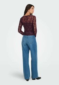 Top de encaje burdeos de manga larga combinado con unos vaqueros de pierna ancha de talle alto en azul claro. Botines negros visibles debajo de los vaqueros.