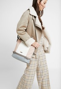 Borsa a blocchi di colore con sezioni rosa, bianca e azzurro chiaro, con hardware grigio e una superficie liscia. Inclusa una tracolla regolabile.