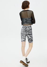 Zwarte mesh cropped top over zebra-print fietsbroek. De outfit heeft een gedurfd zwart-wit patroon, met een losse pasvorm en textuurstof.