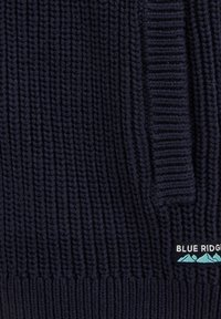 Mornarško modra pletena jopica z navpičnim žametu, ki ima majhno oznako "BLUE RIDGE" z grafiko gore in teksturirano tkanino.