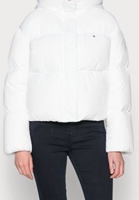 Biała kurtka puchowa o skróconym kroju, z pluszowymi, pikowanymi sekcjami i zapięciem na zamek. Zawiera kaptur oraz logo na rękawie.