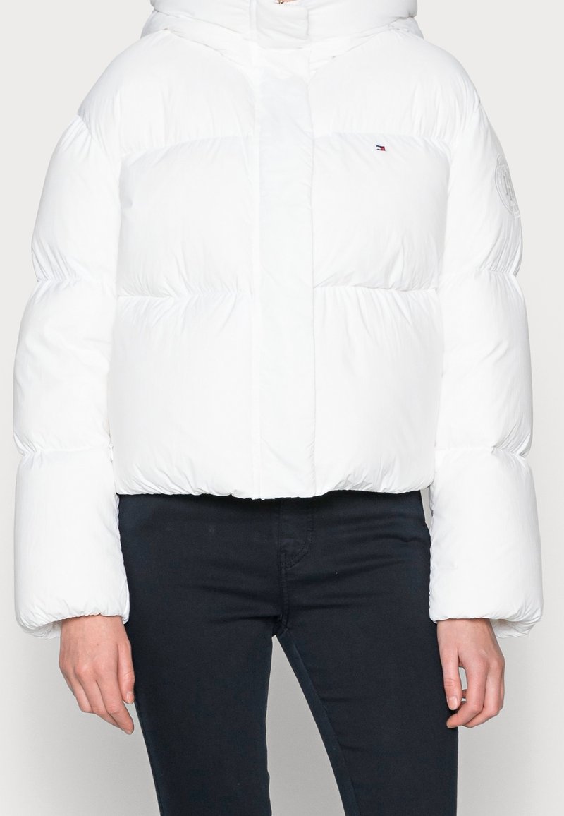 Biała kurtka puchowa o skróconym kroju, z pluszowymi, pikowanymi sekcjami i zapięciem na zamek. Zawiera kaptur oraz logo na rękawie.