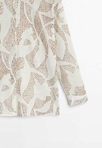 Chemise à manches longues beige clair avec motifs abstraits marron, devant boutonné et texture lisse.