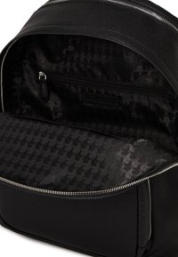 Black leather backpack featuring a textured exterior, silver zipper, and a patterned fabric lining with a zippered interior pocket.